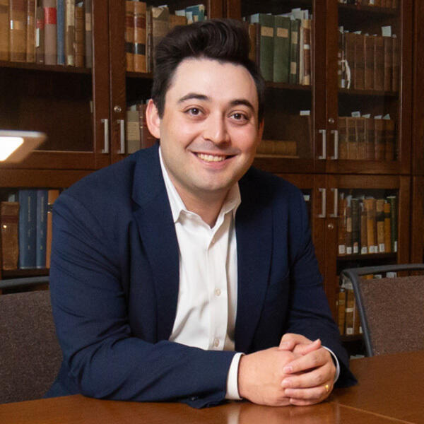 A man in a suit sits with his arms on a wooden table