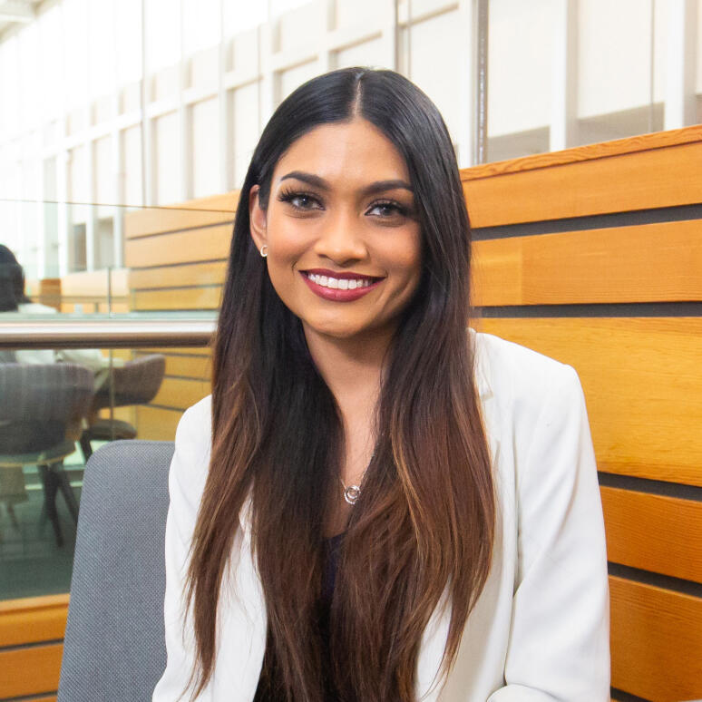 A woman with long brown hair and a white coat smiles at the camera