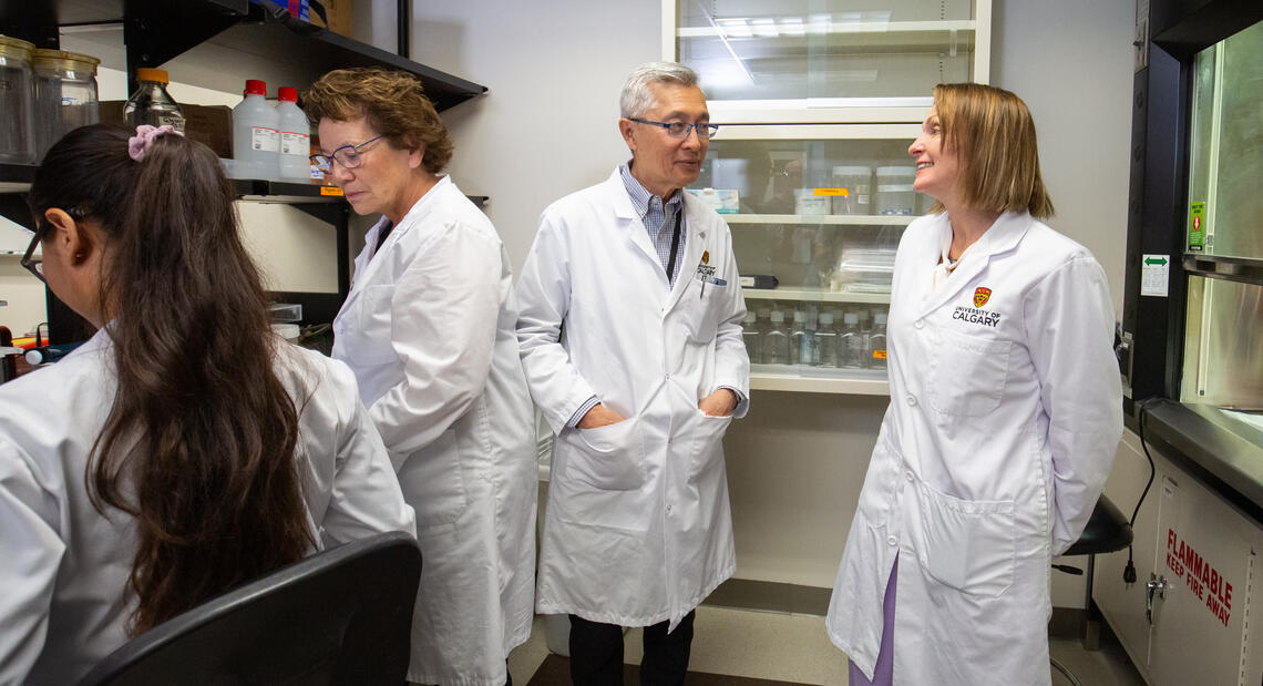 A group of researchers stand in conversation while wearing white lab coats