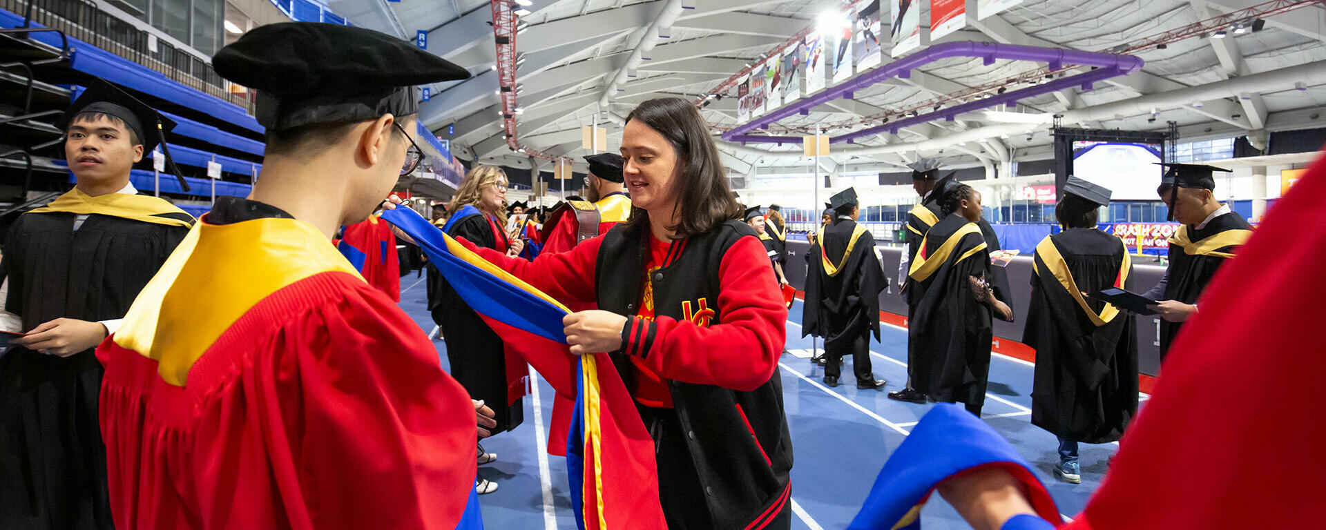 A volunteer helps place a PhD hood on a graduating student