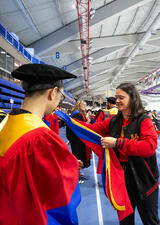 A volunteer helps a student into their hood