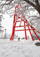 person walking in the snow under the paperclip statue