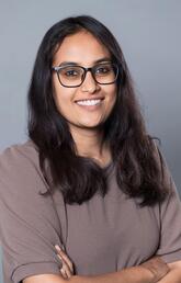 A woman with long dark hair and glasses smiles at the camera