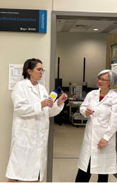Two people stand together wearing white lab coats