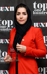 A woman in a hijab holds an award and smiles at the camera