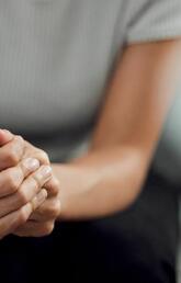 A single person sits in frame with clasped hands in their lap
