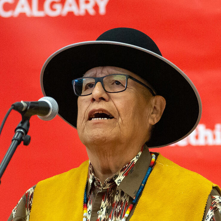 A man wearing a wide brimmed hat sings into a microphone