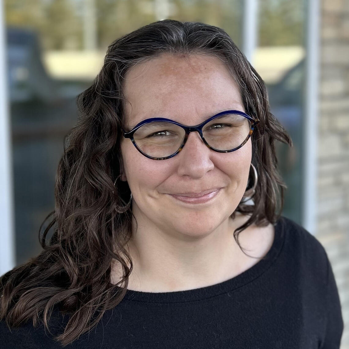 A woman with dark hair and glasses smiles at the camera