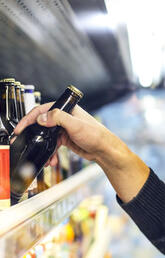 A hand reaches towards a commercial shelf full of beverages, pulling out a single bottle.